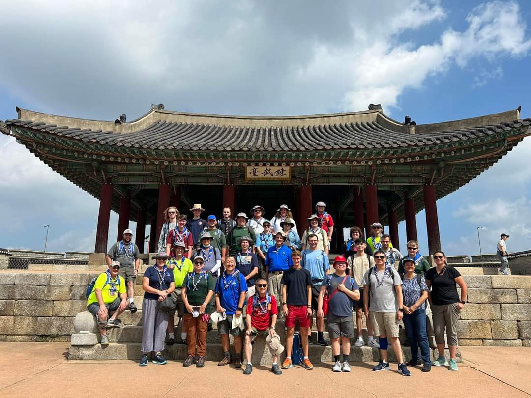A group of people stand in front of a IST in front of a pavilion at Suwon Hwaseong Fortress.